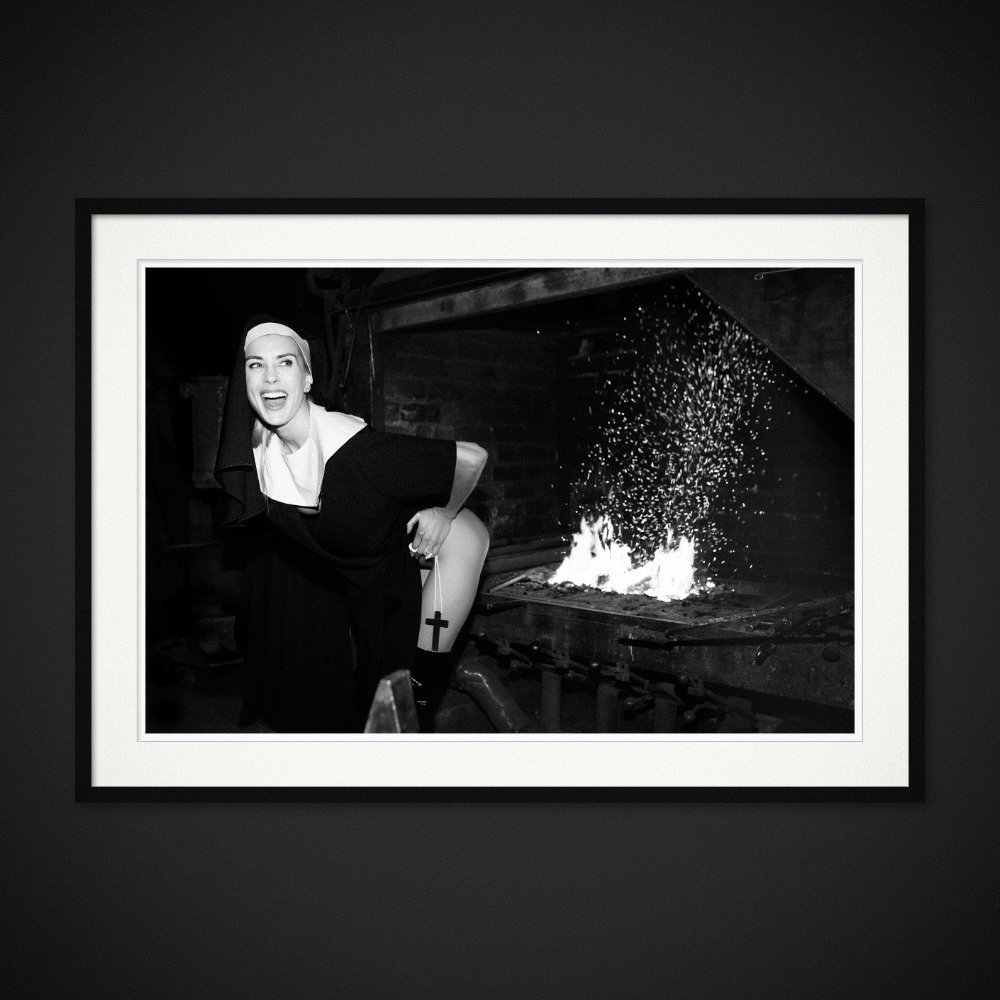 Confession — A nun’s habit, a raised hem and a smile beside the fire. Framing preview by Albert Pocej; frame not included.