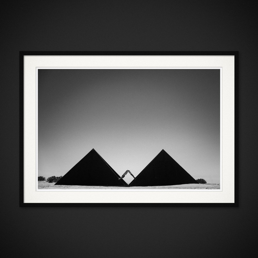 Mind The Gap — A body completes the geometry between two dark triangular structures. Framing preview by Albert Pocej; frame not included.