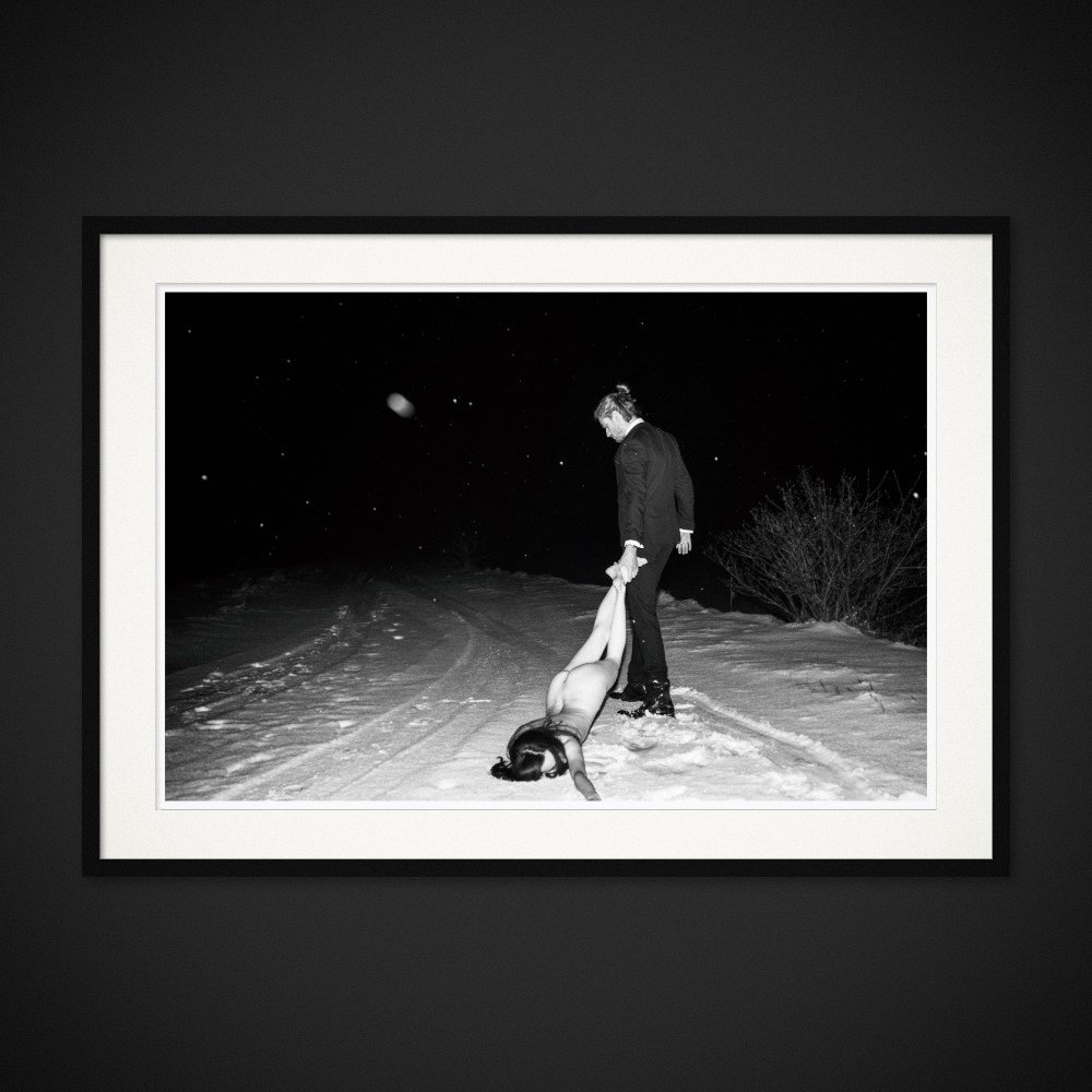 The Pull Of Love — A figure is held by the ankles on a snowy path at night. Framing preview by Albert Pocej; frame not included.